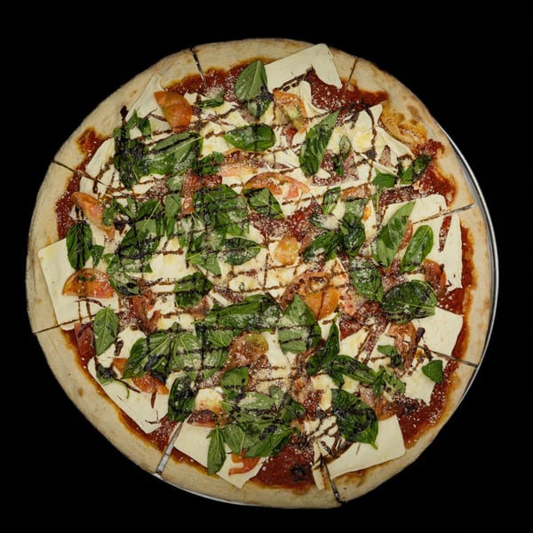 A whole pizza with tomato sauce, mozzarella, fresh basil, and balsamic glaze, sliced on a metal tray.