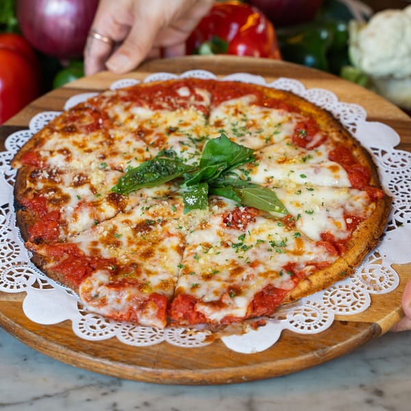 Hands presenting a freshly baked pizza with melted cheese, tomato sauce, and basil on a wooden board.