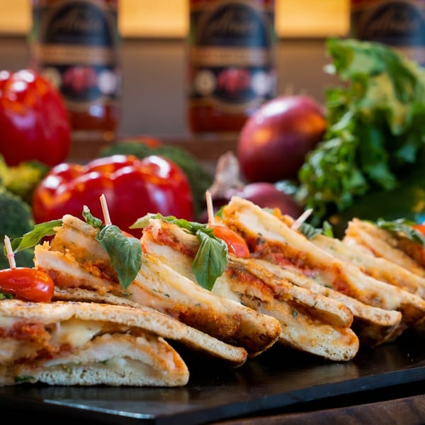 Grilled sandwiches with cheese, tomato, and basil, surrounded by fresh vegetables and sauce bottles.