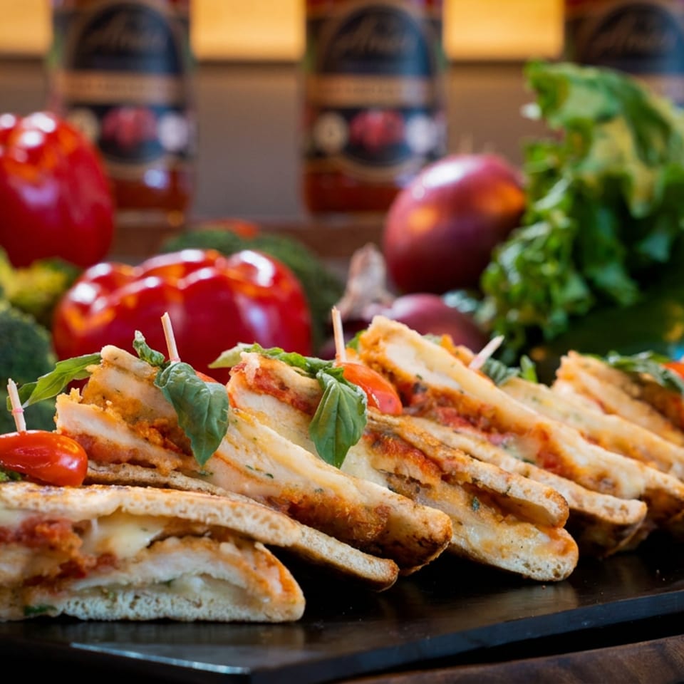 Grilled sandwiches with cheese, tomato, and basil, surrounded by fresh vegetables and sauce bottles.