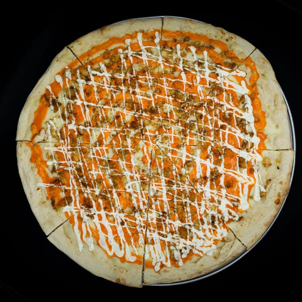 Overhead view of a sliced buffalo chicken pizza with orange sauce and white ranch drizzle.